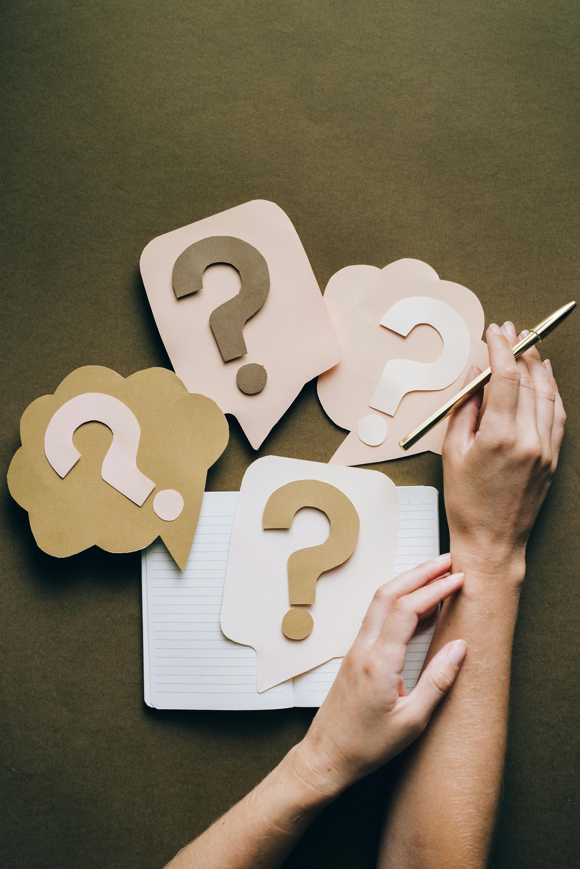 A person is writing on a piece of paper with question marks on it.
