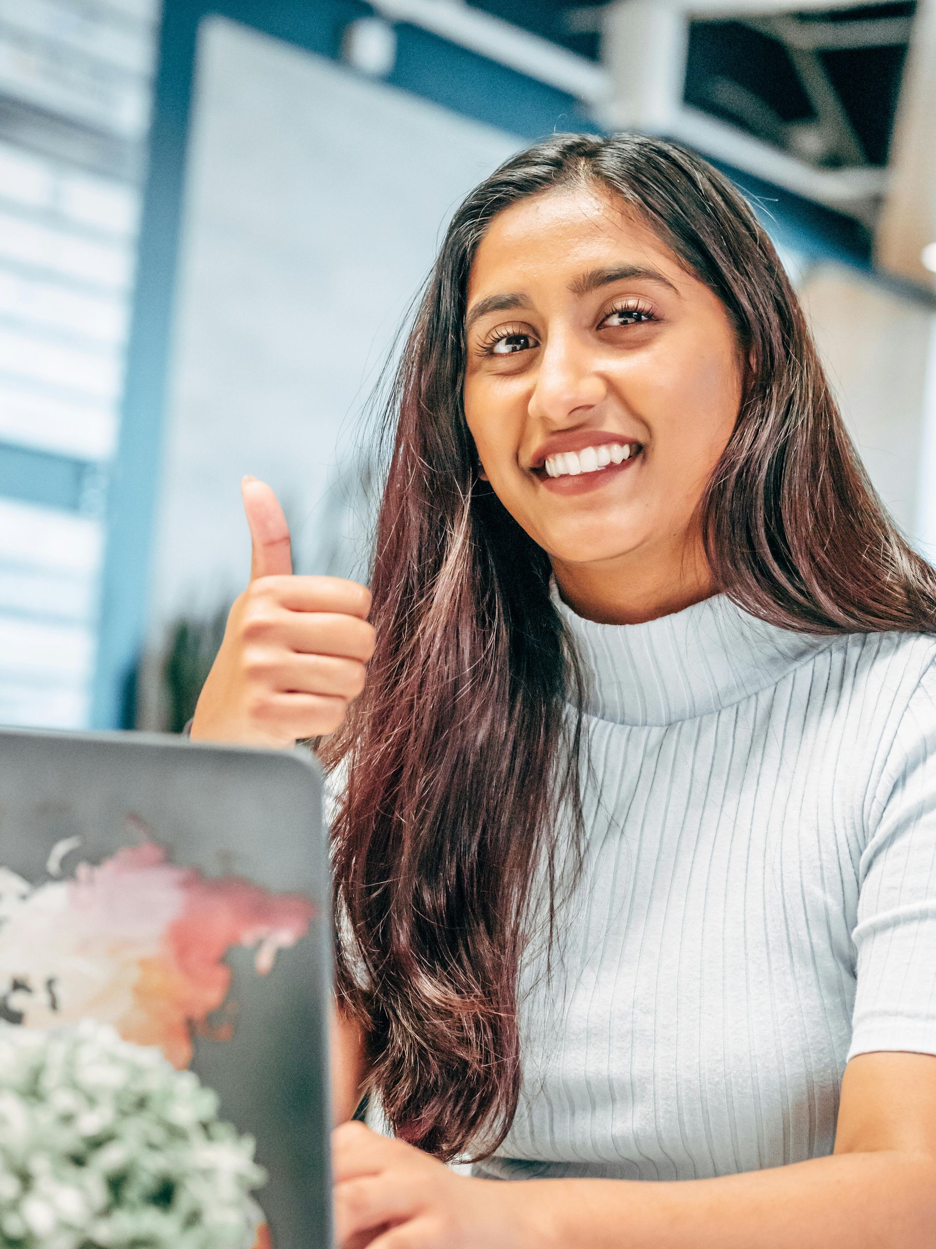 A woman is giving a thumbs up while sitting in front of a laptop computer.