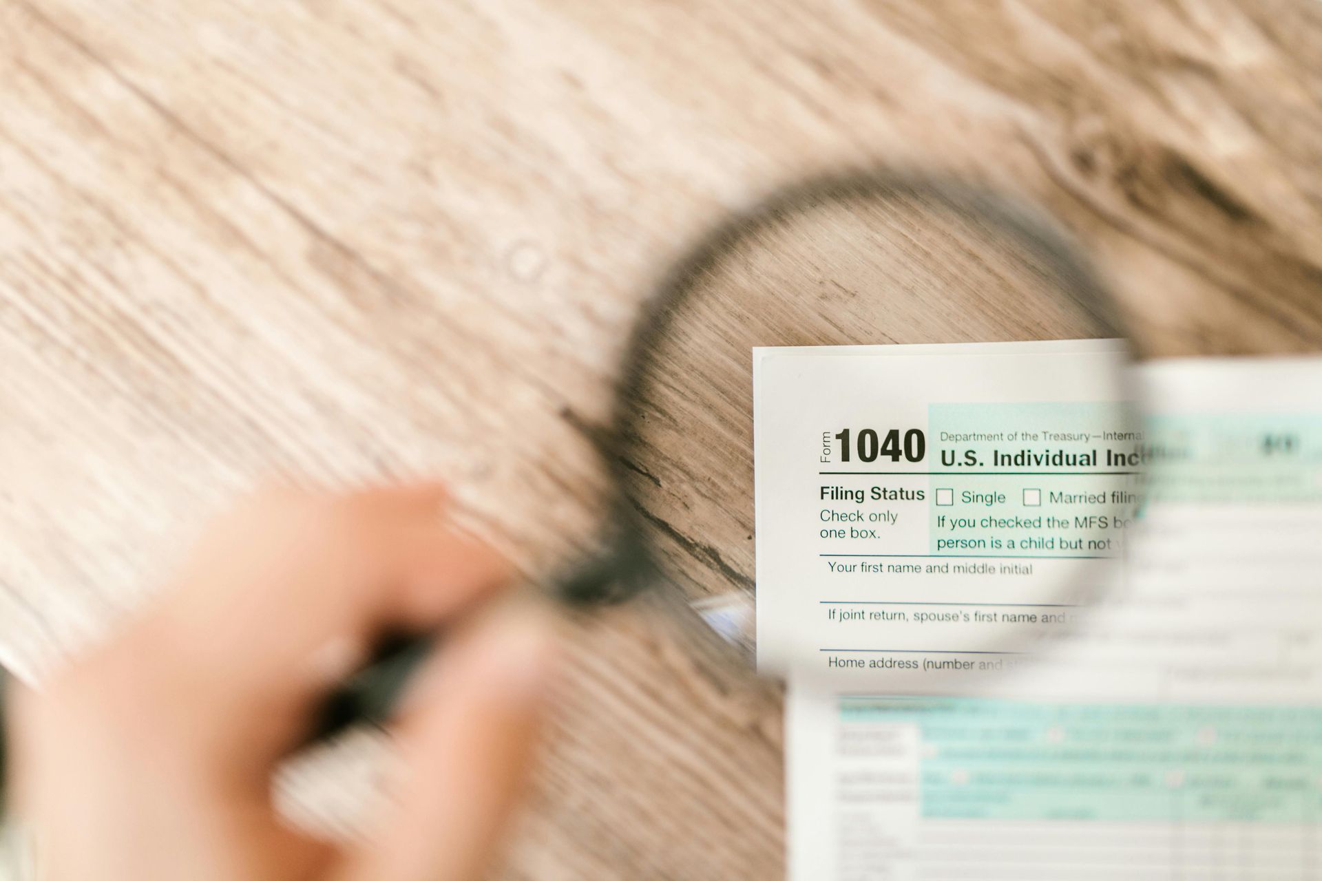 A person is holding a magnifying glass over a tax form.