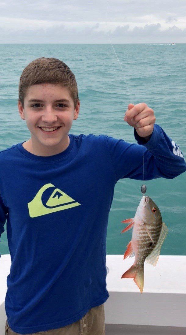 A young boy in a blue shirt is holding a small fish in his hand.