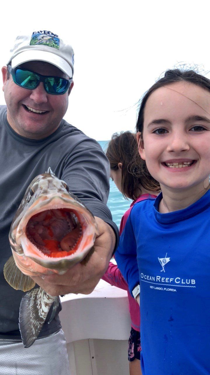 A man and a girl are holding a fish with their mouths open.