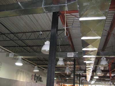 A large building with a lot of ducts and lights hanging from the ceiling.
