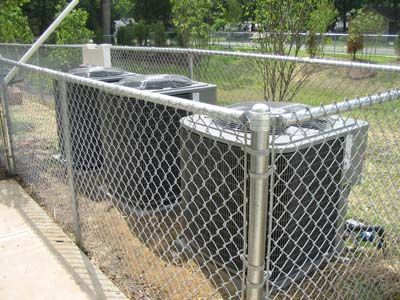 Two air conditioners are behind a chain link fence.