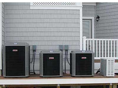 Three air conditioners are sitting on a porch of a house.