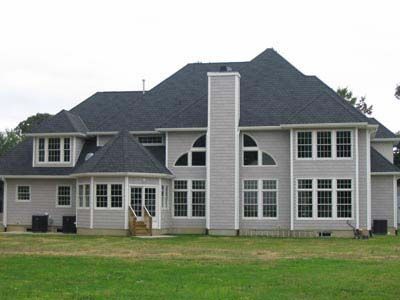 A large white house with a black roof is sitting on top of a lush green field.