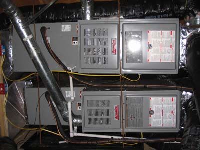 Two air conditioners are stacked on top of each other in a basement.