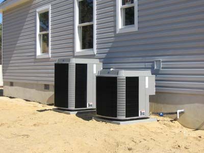 Two air conditioners are sitting on the side of a house.