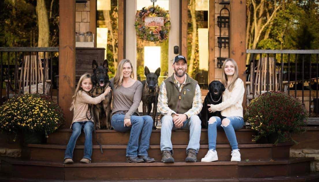 A family is sitting on the steps of a house with their dogs.
