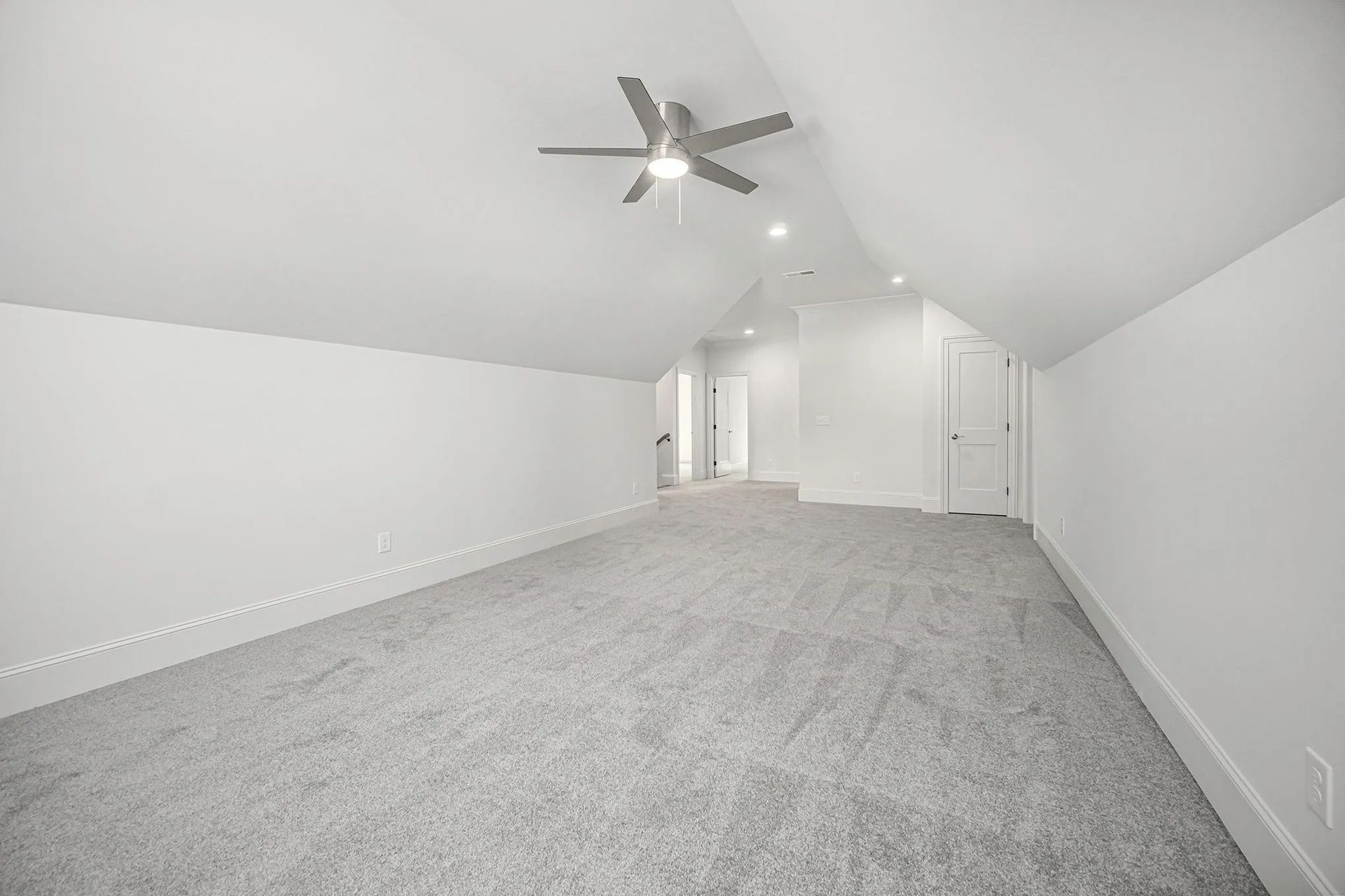 An empty room with a ceiling fan and a gray carpet.