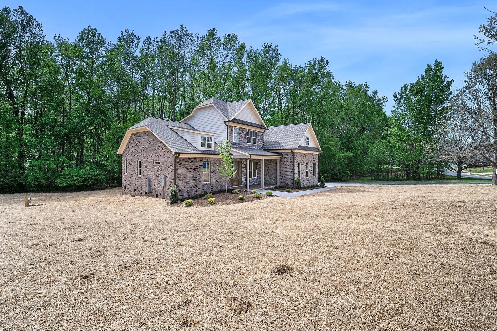 A large brick house sits in the middle of a dirt field