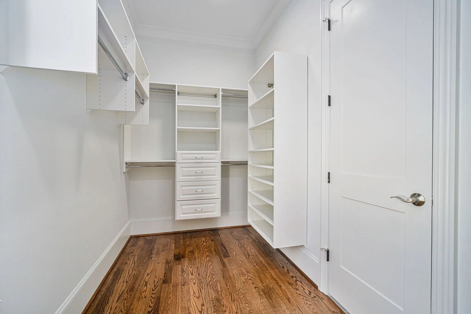 A walk in closet with hardwood floors and white cabinets.