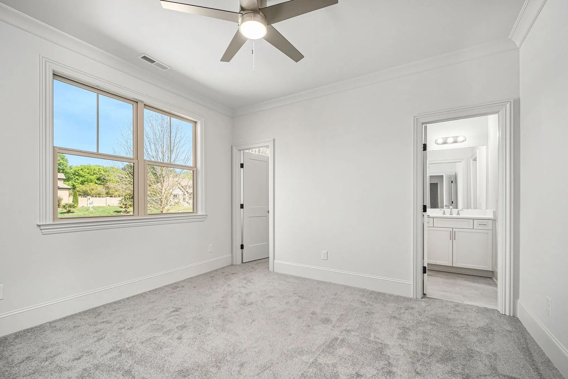 An empty bedroom with a ceiling fan and two windows.