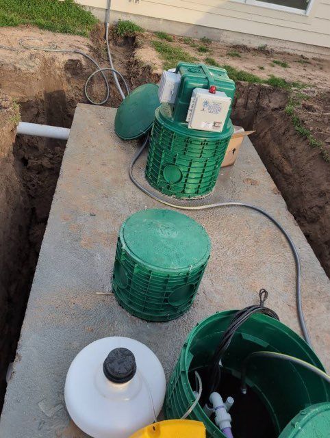 Septic system components in an excavated trench: green tanks, white and black containers, wires.