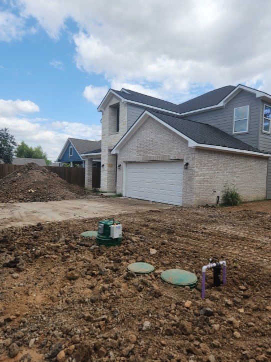 New house under construction; light brick, two-story, with garage. Brown dirt foreground, blue sky.