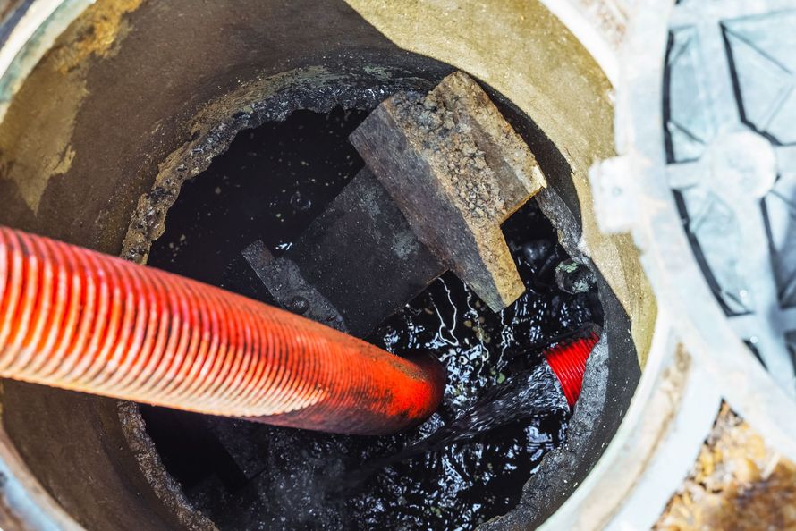 Inside a sewage manhole, a red hose is submerged in dark, thick sludge.