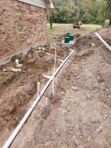Construction site: Trench with white pipes, a septic tank, and a brick building.