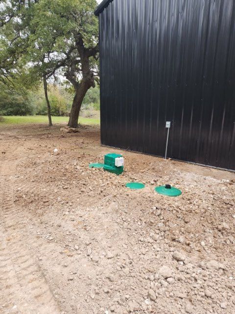 Concrete septic tank with open lid and green hose, in grassy backyard near an AC unit.