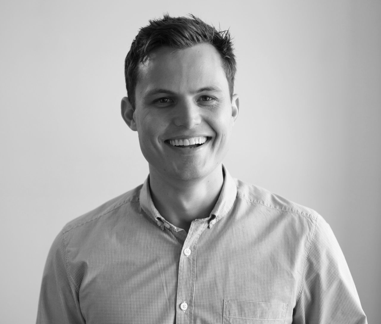 A man in a plaid shirt is smiling in a black and white photo.