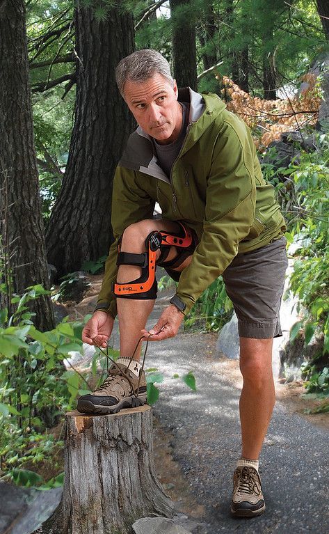 a man wearing a knee brace is tying his shoelaces on a tree stump .
