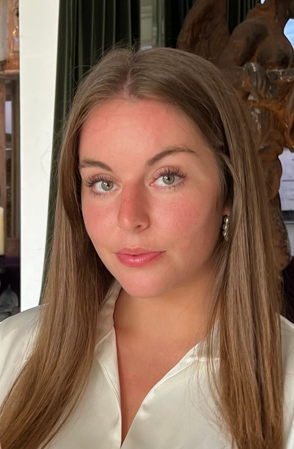 A woman with long brown hair is wearing a white shirt and earrings.