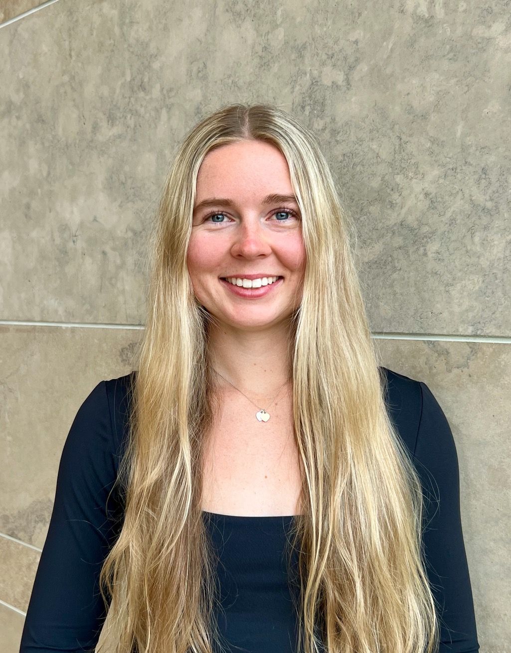 A woman with long blonde hair is wearing a black shirt and smiling.