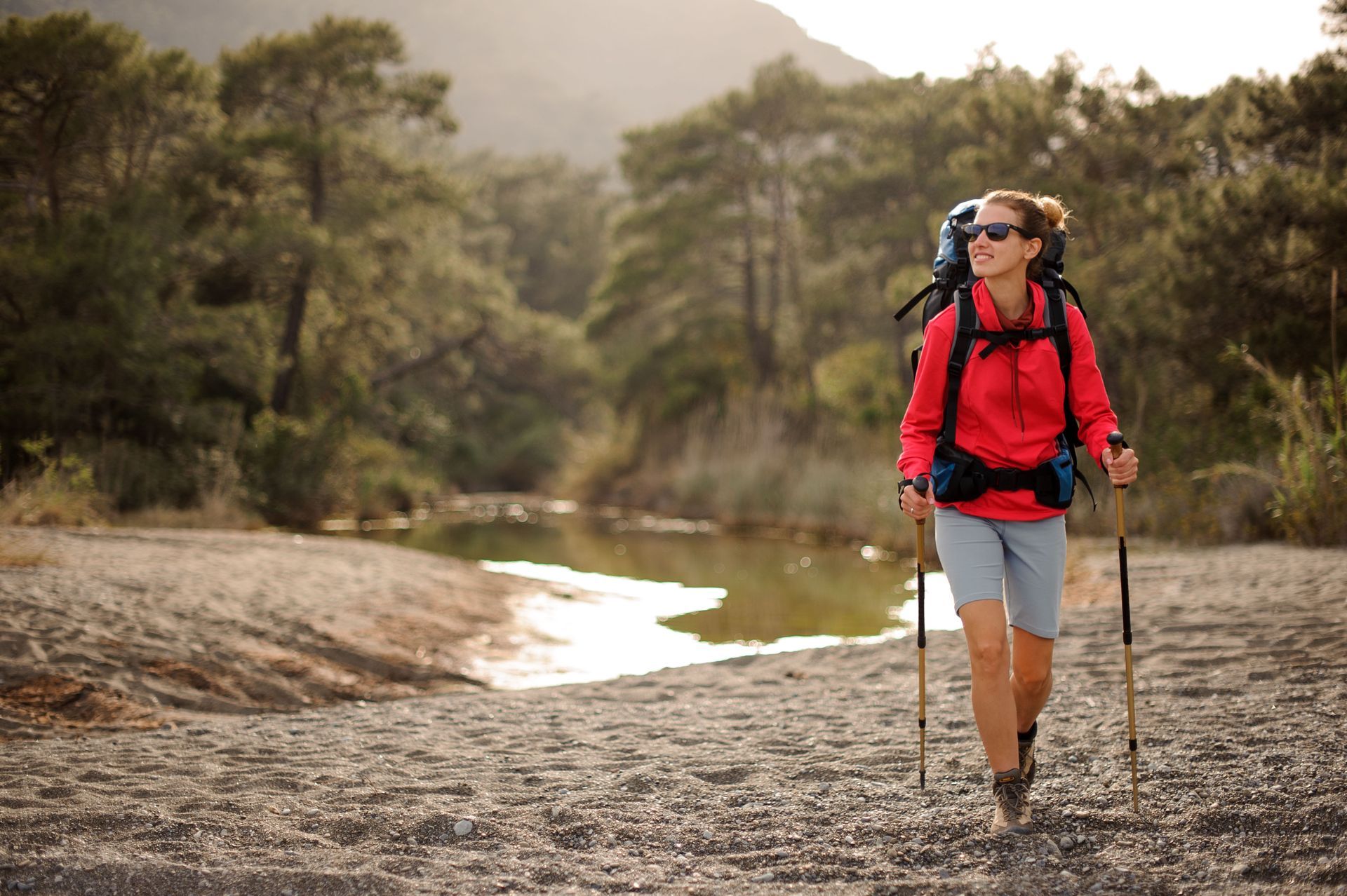 a woman with a backpack and hiking poles is walking along a river .