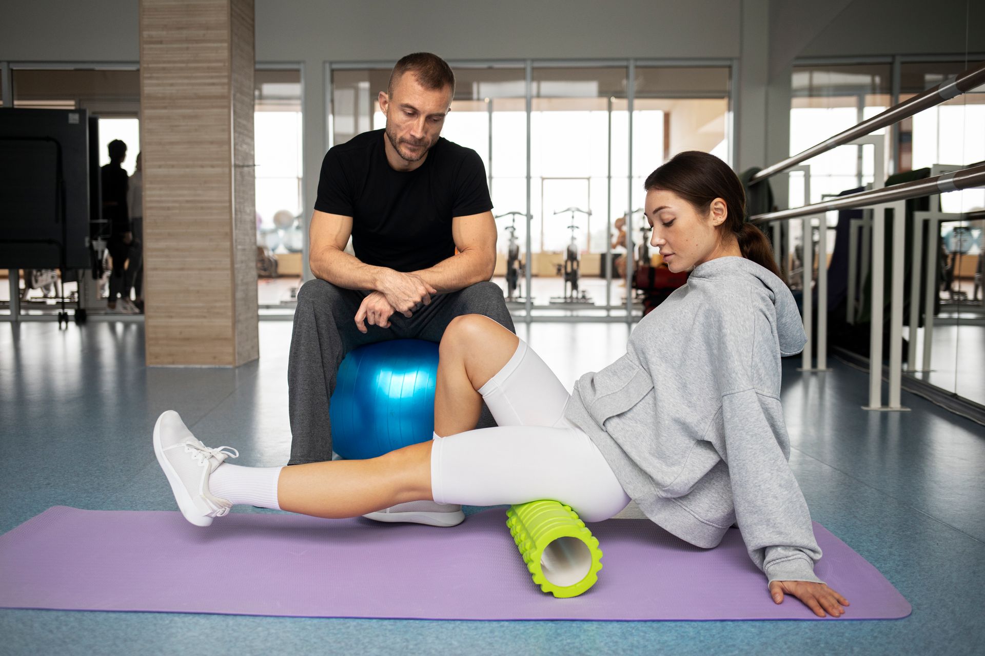 A man is sitting on a blue ball while a woman is laying on a yoga mat.