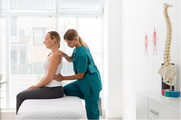 A woman is sitting on a bed getting a massage from a nurse.