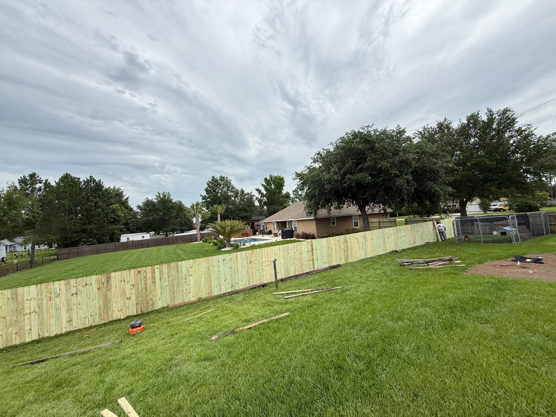 Newly built wooden fence in a grassy backyard, cloudy sky overhead, home in the background.