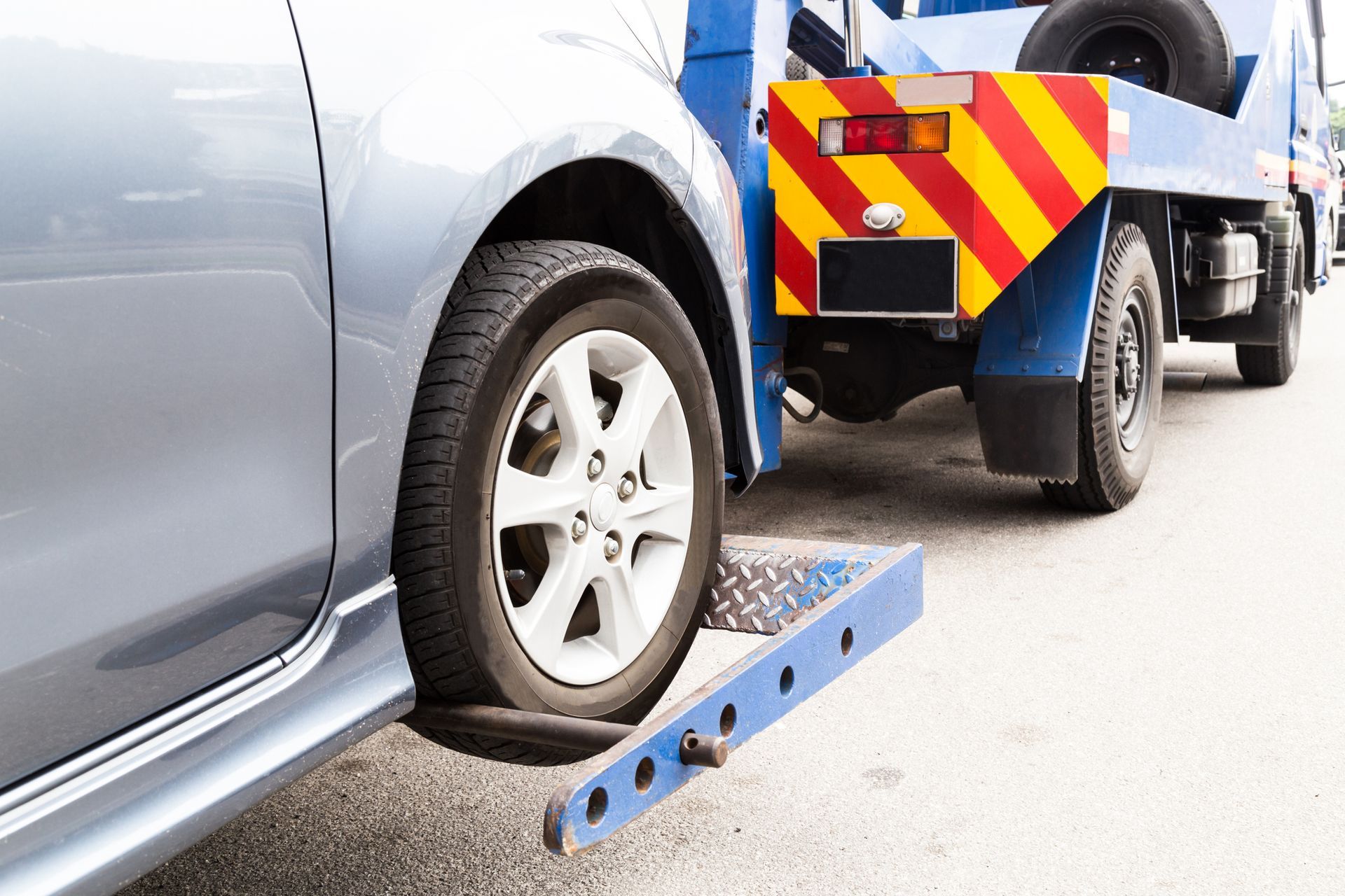 Tow truck loading silver car onto flatbed for roadside assistance and vehicle recovery service/