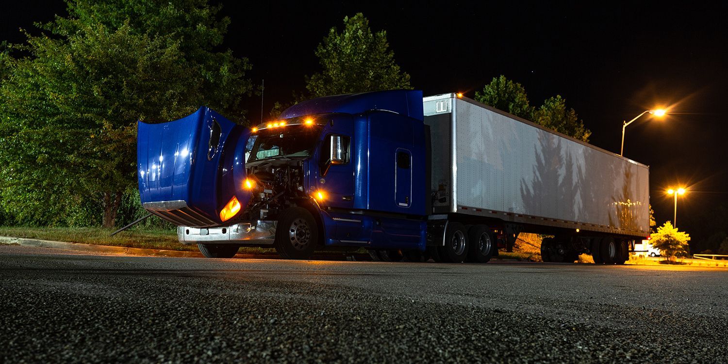 Blue semi-truck parked at night with its hood open under streetlights.