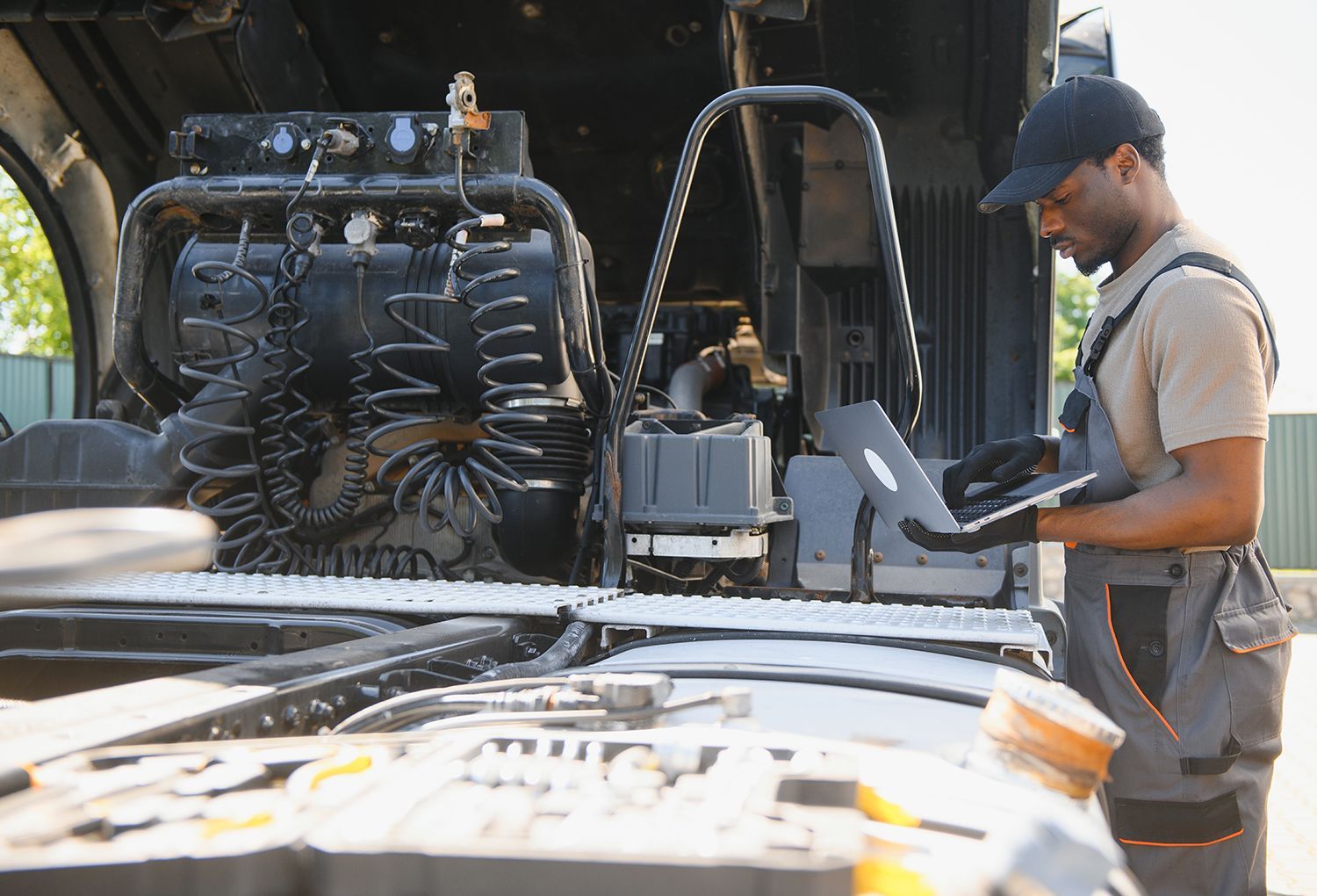 Mechanic using a laptop while inspecting the engine components of a large truck. Mechanic using a laptop while inspecting the engine components of a large truck.