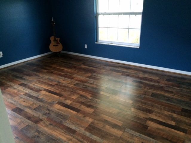 A guitar is sitting in the corner of a room next to a window.