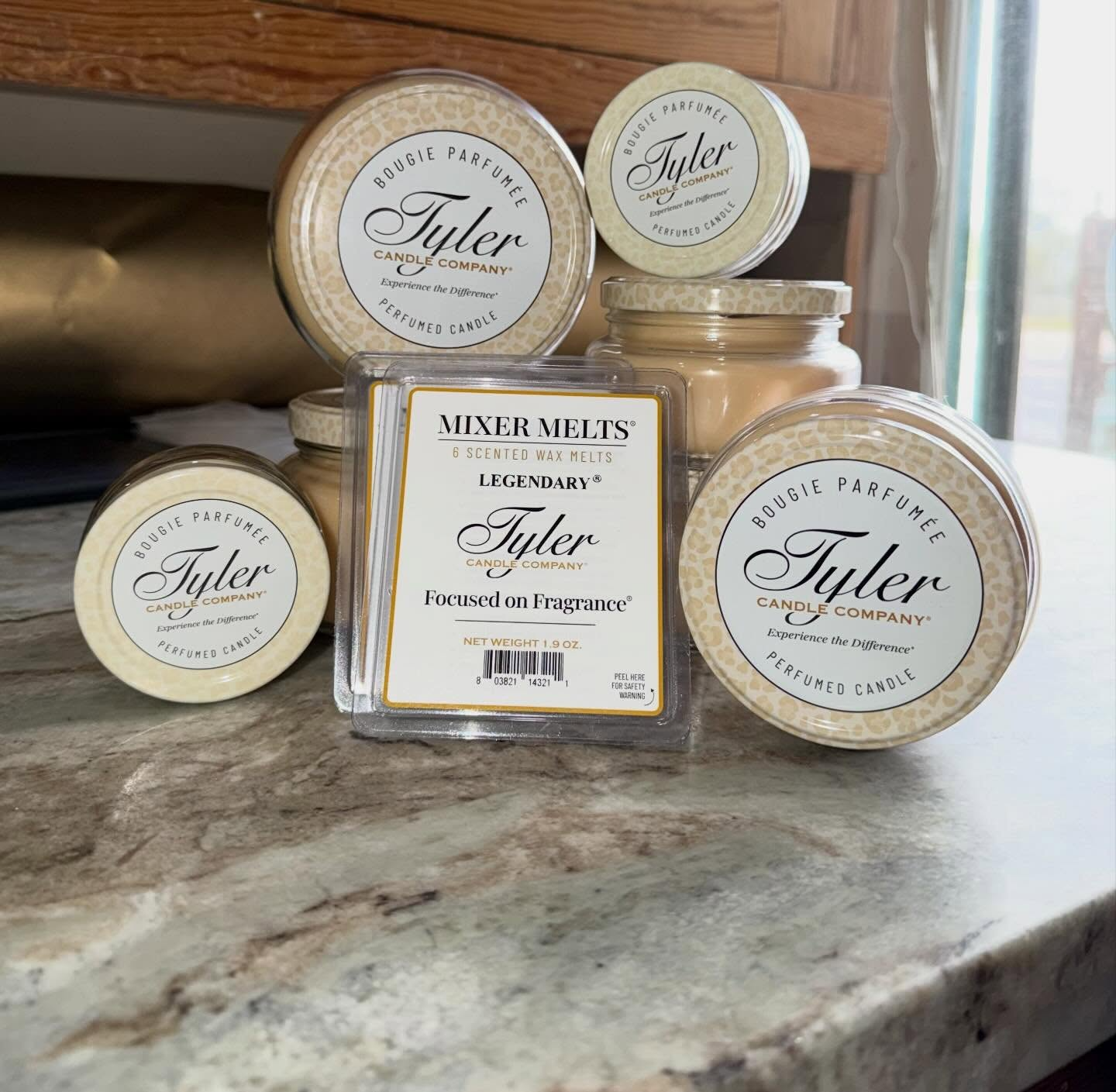 Assorted Tyler candle jars and a square scented candle on a marble countertop near a window