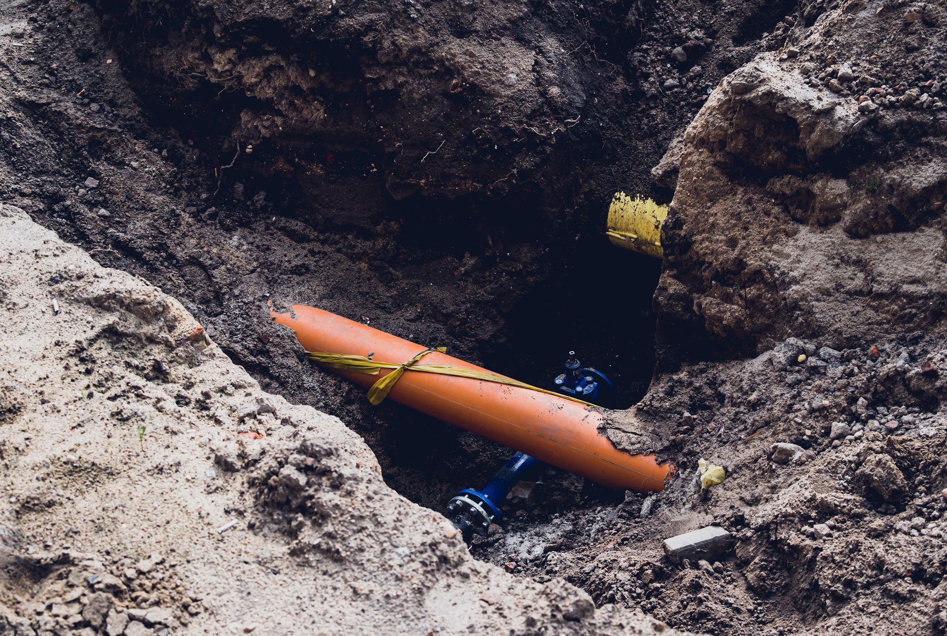 Exposed sewer line under repair in deep trench showing orange drainage pipe and soil. Exposed sewer line under repair in deep trench showing orange drainage pipe and soil.