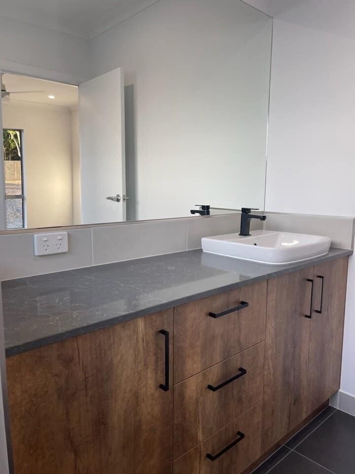A Bathroom With A Sink, Mirror And Wooden Cabinets — North Coast Cabinetmaking Pty Ltd In Proserpine, QLD