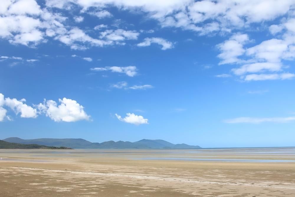 A Beach With Mountains In The Background And A Blue Sky With Clouds — North Coast Cabinetmaking Pty Ltd In Cannonvale, QLD