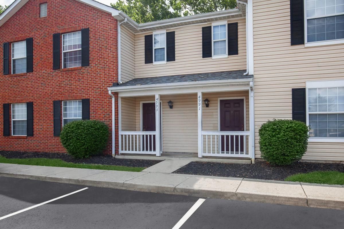Townhouse complex, tan and brick buildings with black shutters, front porches, and parking area.