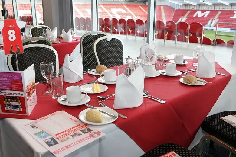 Conference room with a wooden table and chairs overlooking a blue stadium through large windows