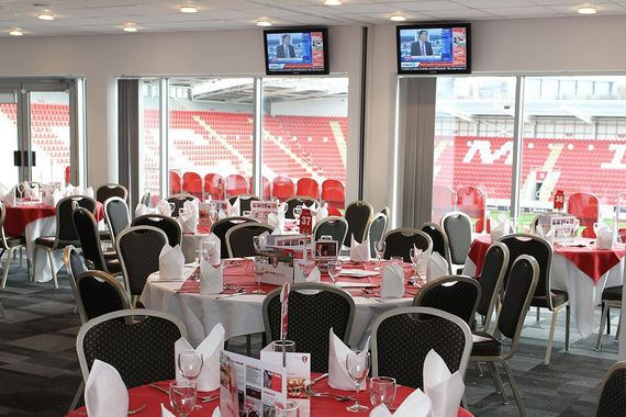 Empty stadium dining area with round tables, black chairs, and TVs overlooking red bleachers
