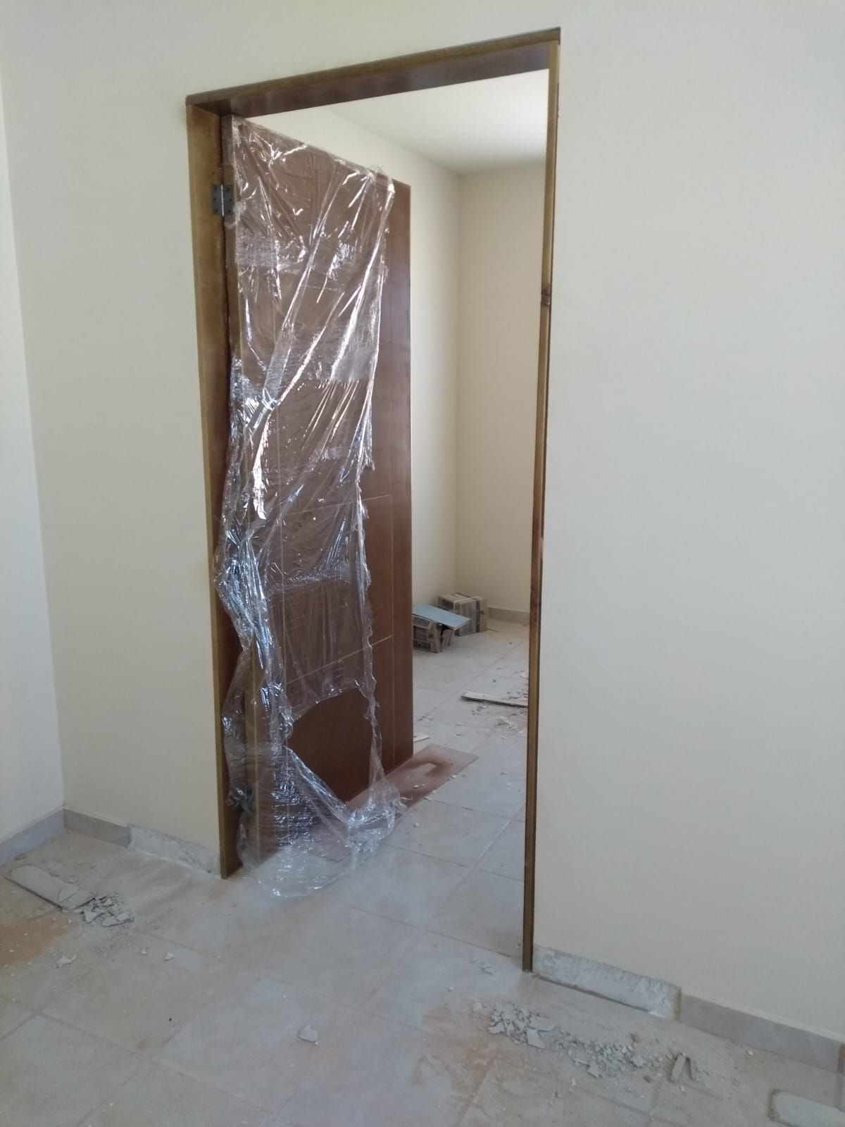 Puerta abierta con puerta marrón envuelta, paredes de color marrón claro y un área de construcción en el interior.