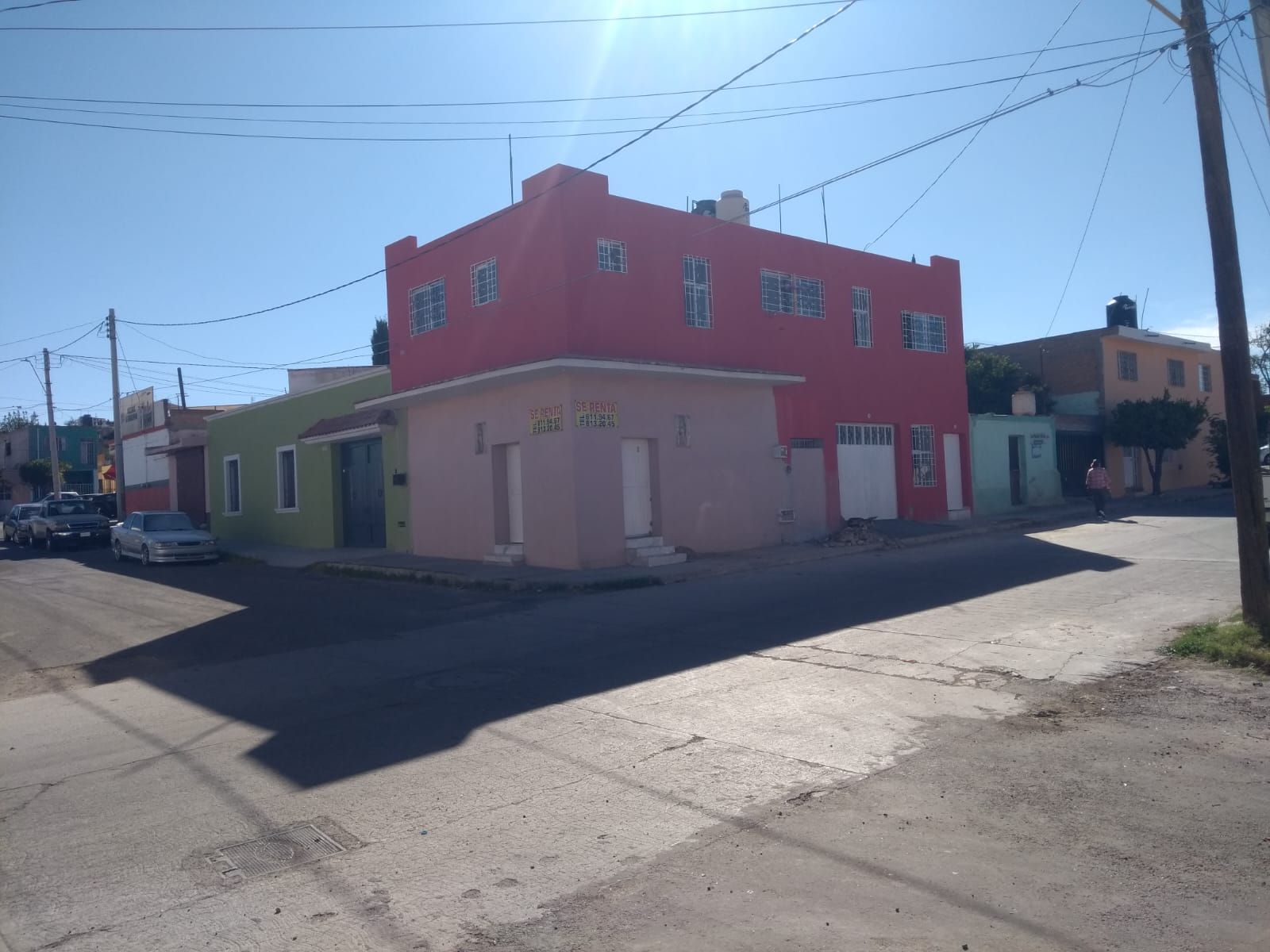 Un colorido edificio de dos pisos con un nivel superior de color rojo y un nivel inferior de color bronce en una esquina soleada de la calle.