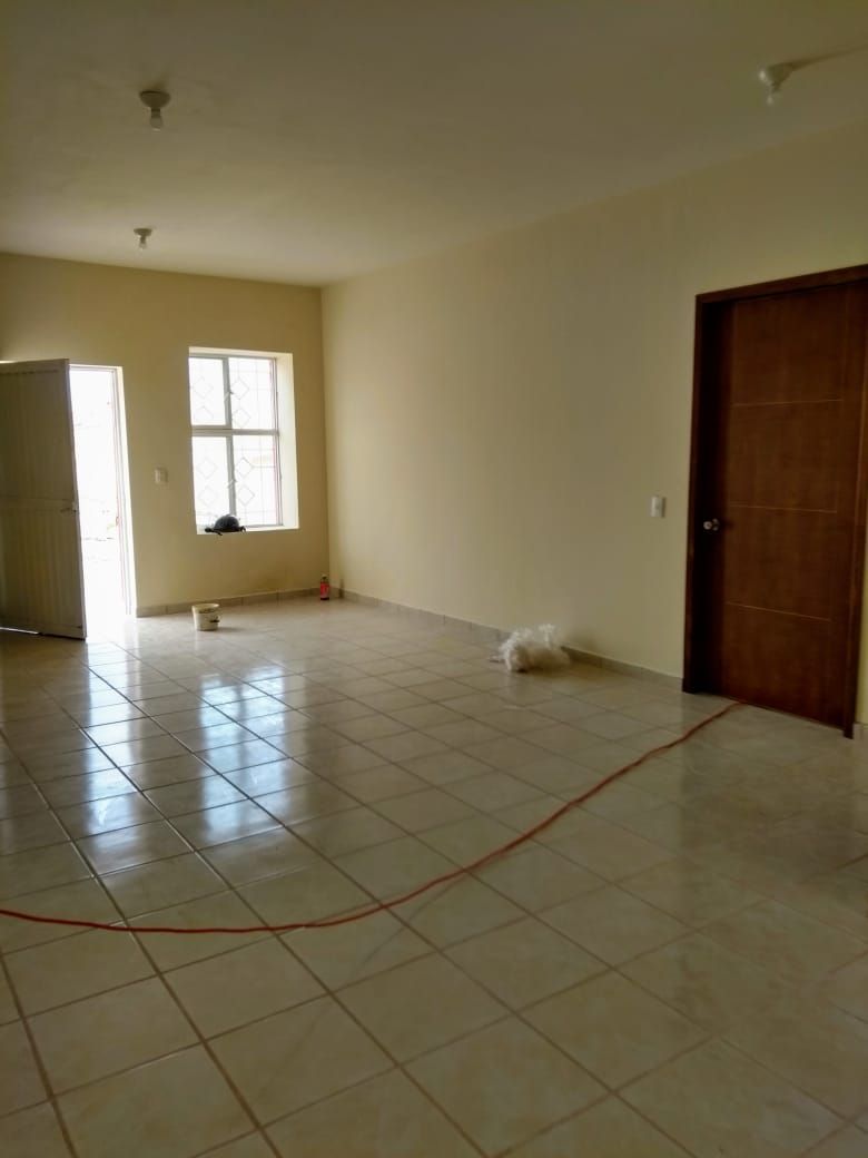 Habitación vacía con suelo de baldosas, puerta abierta, ventana y puerta cerrada; paredes neutrales.