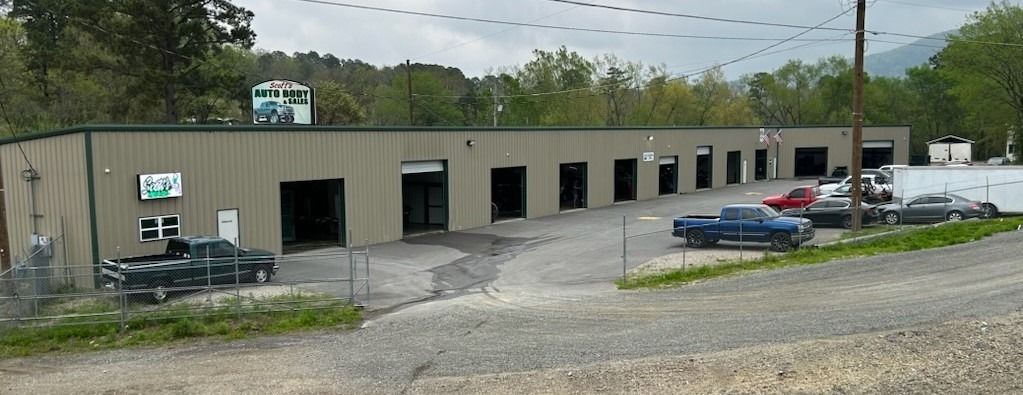 Industrial warehouse with open garage bays, parked cars, and gravel lot under cloudy sky