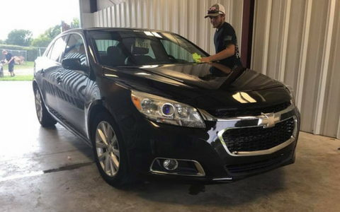 Black Chevrolet sedan in a garage with a man standing beside the driver’s door