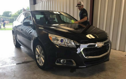 Black Chevrolet sedan in a garage with a man standing beside the driver’s door