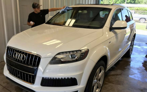 White Audi SUV being wiped down by a person in a car wash bay