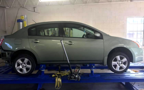 Green sedan on an auto lift in a garage, with a wheel alignment tool attached