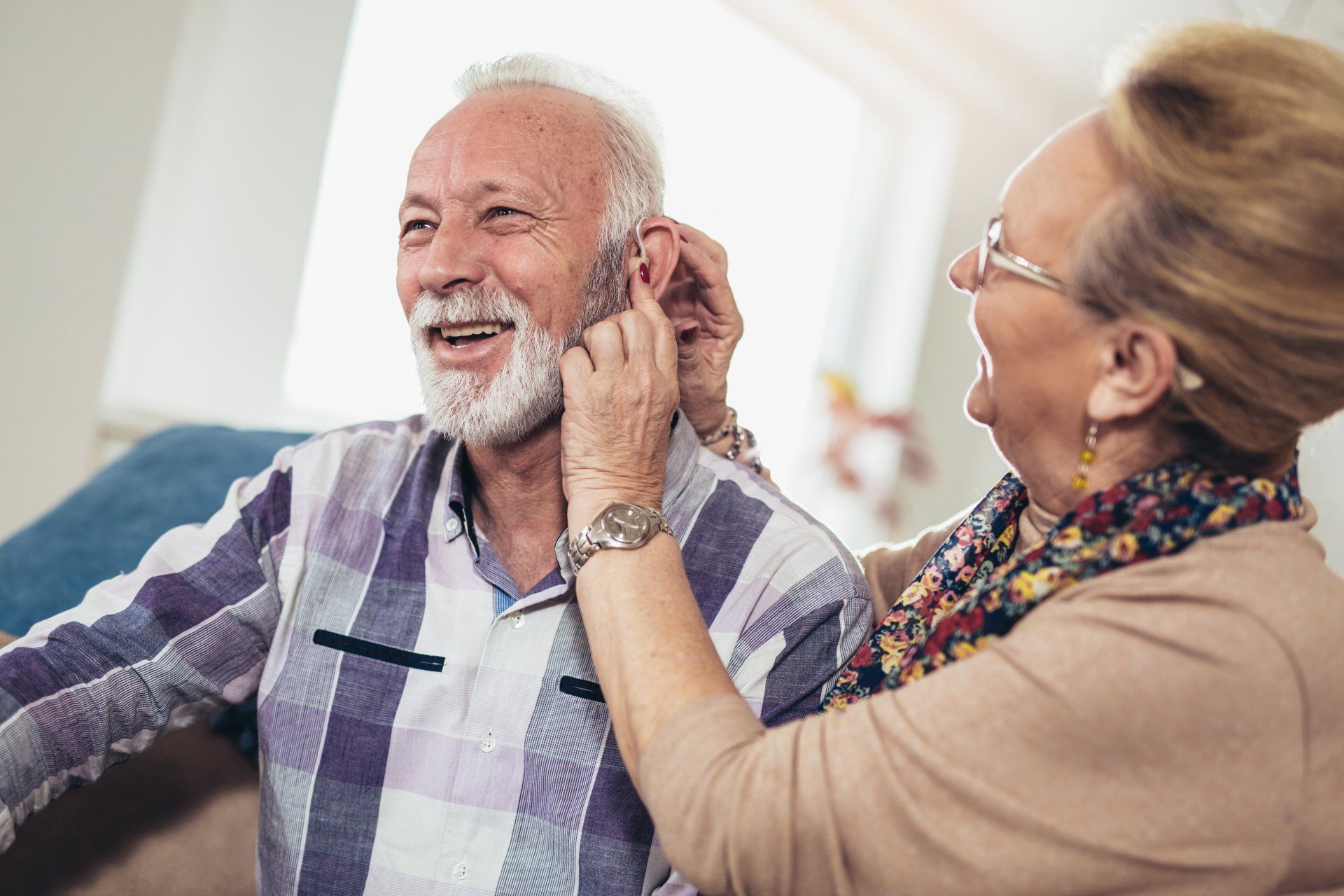 A woman is putting a hearing aid in an older man 's ear.