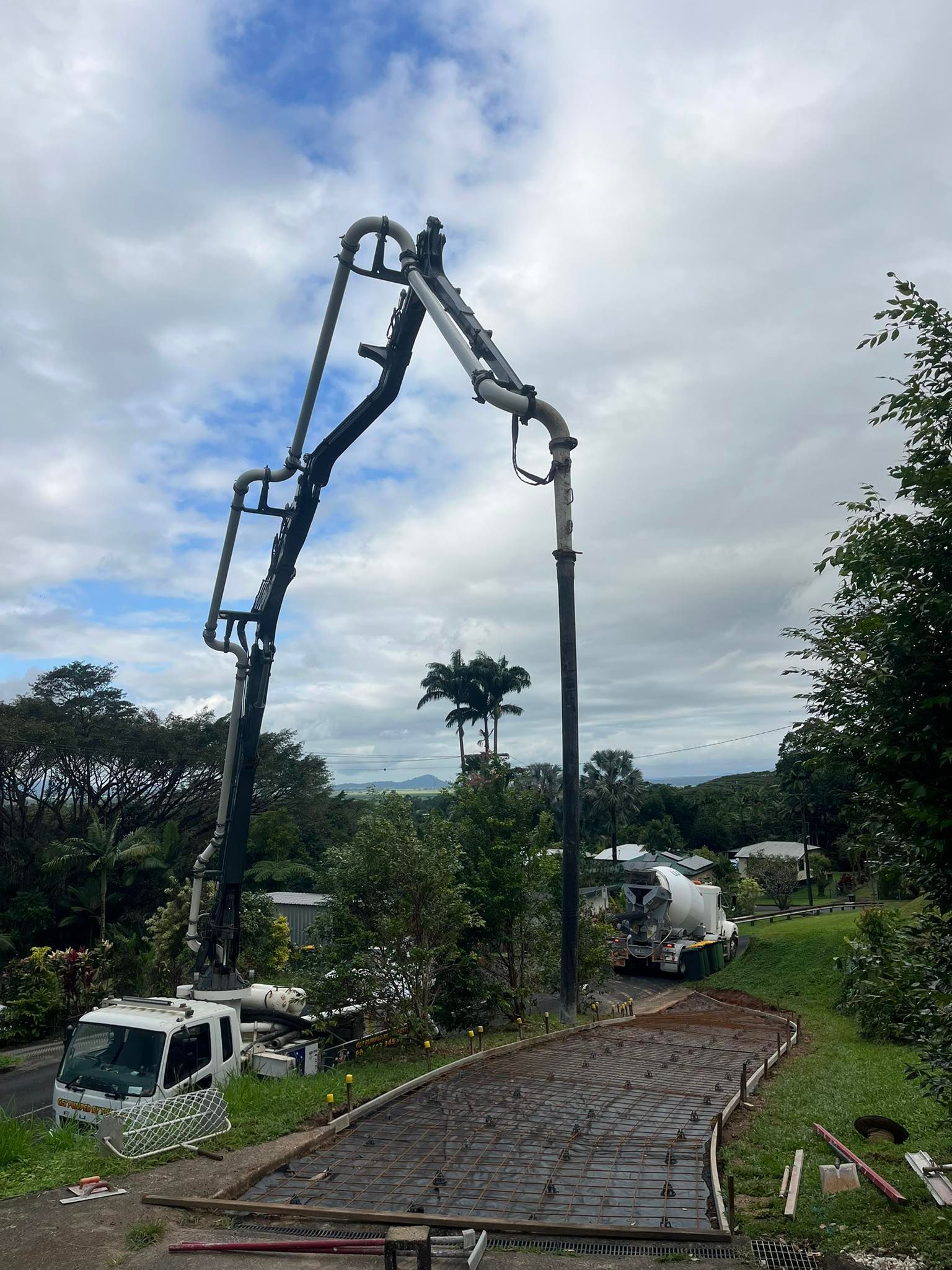 A concrete pump truck extends its boom over a grassy hill to pour wet concrete into a curved, prepared pathway below — Value Concreting In Innisfail, QLD
